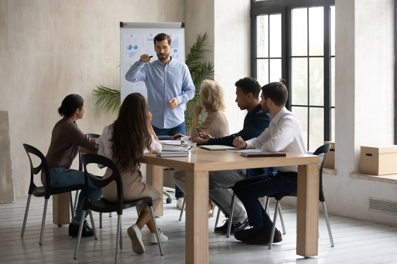 Serious business coach making flip chart presentation, training diverse staff